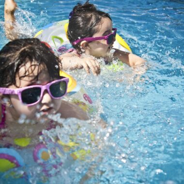 Two young girls enjoying a playful day in a bright blue swimming pool with colorful float rings.